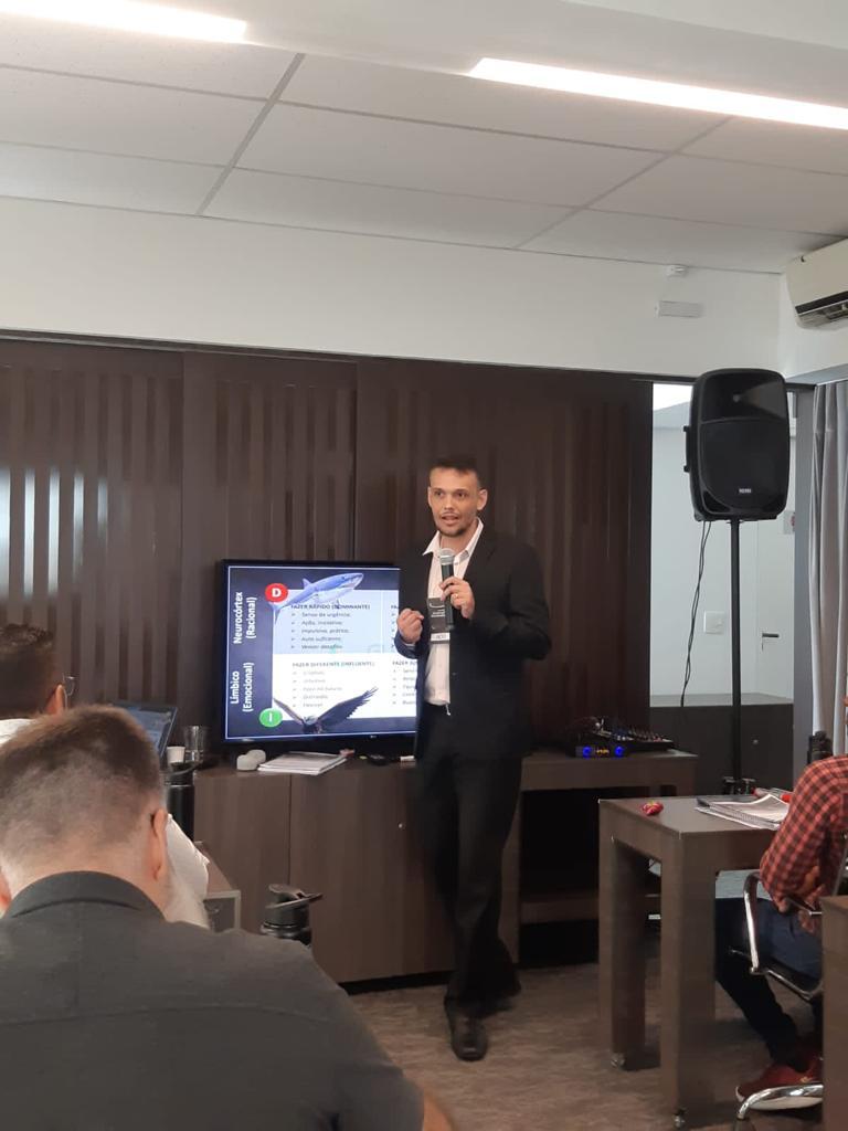 André Lázaro conduzindo uma palestra com microfone e apresentação para empresários